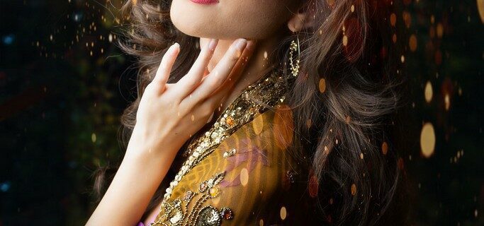 Woman in an ornate gold shawl with intricate embroidery, looking up with soft light on her face, and glittery particles surrounding her